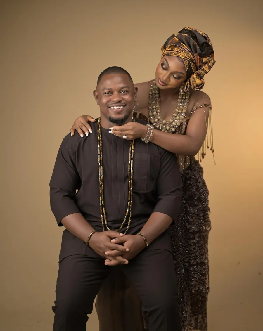 Emma leaning over Kelvin's shoulder, both smiling, in traditional attire
